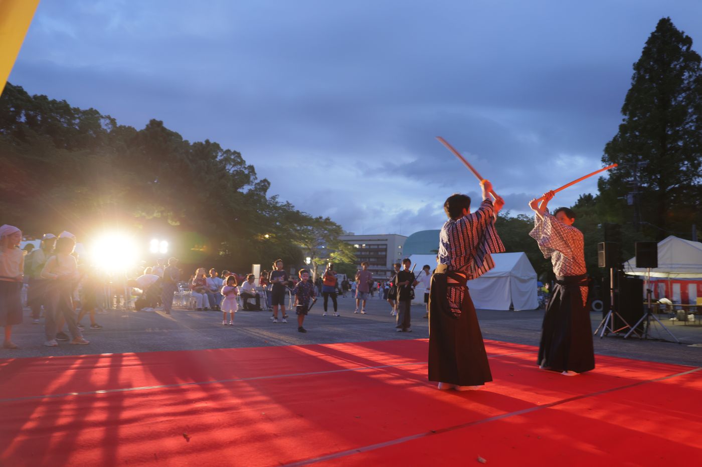 赤い絨毯の上で、木刀を構えて立ち回りの型を披露する二人の演者